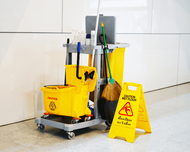 Professional janitorial cleaning trolley with mop, broom, and wet floor sign prepared for emergency cleaning services in a commercial building.